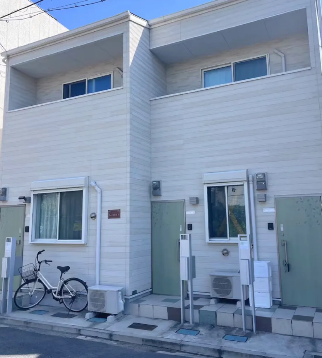 the façade in full sun: two floors, the loggias, and the door at street level